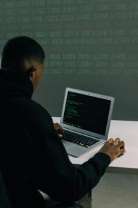 An individual working on a laptop with code displayed on the screen, symbolizing cybersecurity measures.